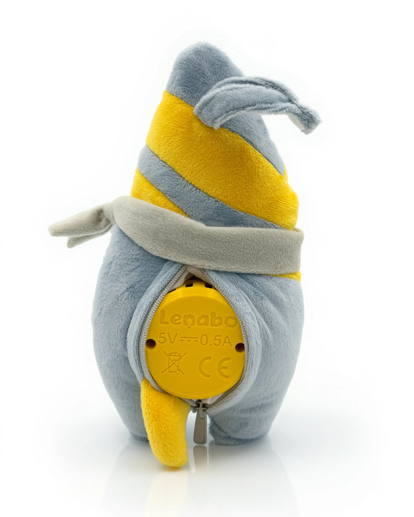 Der Plüschcharakter Nalu aus der Lenabo Inselwelt von hinten. Sein graublauer Körper mit zwei diagonalen gelben Streifen ist am Rücken geöffnet. Durch den Reißverschluss ist der eingesetzte gelbe Lenabo Smart Speaker sichtbar, auf dem technische Angaben wie '5V — 0.5A' zu sehen sind.