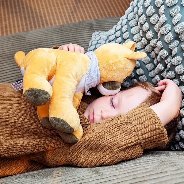 Ein Kind liegt schlafend auf einem Sofa, umgeben von strukturierten Kissen. Es hält den gelben Plüschpuma Tali eng an sich, dessen Kopf am Gesicht des Kindes liegt.