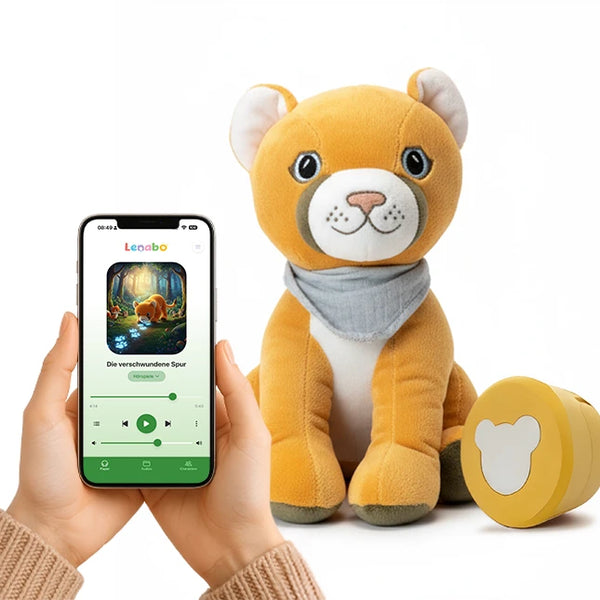 Der gelbe Plüschpuma Tali sitzt vor weißem Hintergrund. Daneben liegt sein gelbes Audiomodul. Zwei Hände halten ein Smartphone mit der Lenabo-App, auf der eine Hörspielgeschichte mit Tali angezeigt wird.